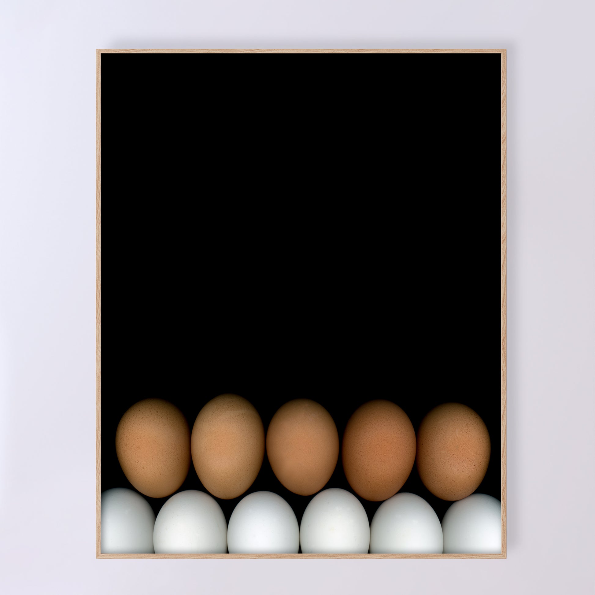 Two rows of chicken eggs one brown row and one white row on a black background in a light beige wood frame. Open edition print by Carmen Grenier. OE-355-3, 16x20 inches.