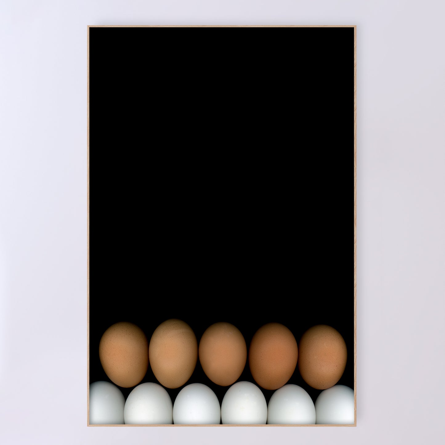 Two rows of chicken eggs one brown row and one white row on a black background in a light beige wood frame. Open edition print by Carmen Grenier. OE-355-4, 24x36 inches.